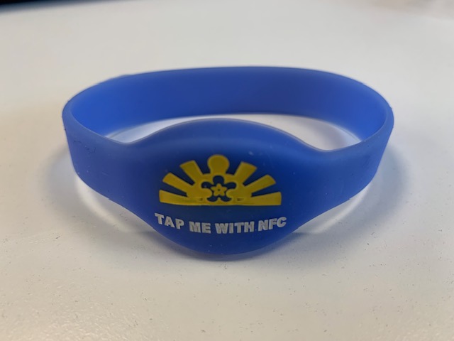 a dementia buddy wrist band - blue with a yellow pattern and text saying "tap me with nfc"